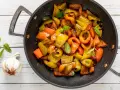 Peperoni in padella, colorati e succosi, con foglie di menta fresca e uno spicchio d'aglio.