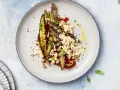 Deliziosa insalata di melanzane grigliate con feta sbriciolata, pomodoro, noci e semi di sesamo nero, condita con olio d'oliva.
