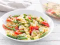 Un piatto invitante di pasta fredda vegana con farfalle, pomodorini, zucchine e fagiolini. Perfetta per un pasto leggero e gustoso.