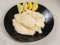 Scaloppine di pollo al limone, un piatto classico e saporito, servite su un piatto nero con spicchi di limone fresco.
