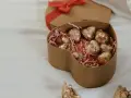 Scatola a forma di cuore con cioccolatini fatti in casa dorati su paglia rosa. Un'altra scatola a forma di cuore con fiocco rosso è sullo sfondo.