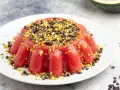 Delizioso gelo di melone rosso, guarnito con gocce di cioccolato e pistacchi tritati, su un piatto bianco.