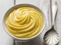 Una ciotola di soffice crema pasticcera, pronta per essere gustata. Accanto, un cucchiaio d'argento.