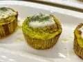 Tre tortini di zucchine dorati, guarniti con formaggio fuso e aneto, serviti su un piatto bianco.
