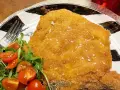 Una dorata cotoletta alla milanese, croccante e cosparsa di sale grosso, servita con un'insalata fresca di rucola e pomodorini.