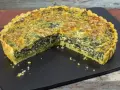 Una fetta di torta salata ricotta e spinaci, con crosta dorata e ripieno cremoso, su una lavagna scura.