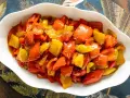 Peperoni in umido, colorati e succulenti, conditi con erbe aromatiche, serviti in una ciotola bianca su un tovagliolo decorato.