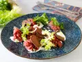 Deliziosa tartare di manzo con lattuga croccante, capperi e una crema bianca su un piatto blu decorato.