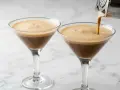 Due bicchieri di **caffè shakerato** con una schiuma densa e invitante. Uno viene riempito da uno shaker.