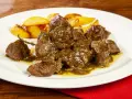Un saporito abbacchio alla cacciatora, tenero e succulento, servito con patate arrosto su un piatto bianco.