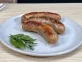 Tre salsicce dorate in padella, servite su un piatto con rosmarino e alloro.