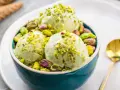 Tre palline di cremoso gelato al pistacchio, guarnite con granella e pistacchi interi, in una ciotola blu.