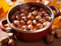 Castagne bollite con buccia in una pentola rossa, circondate da foglie autunnali.