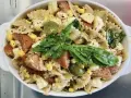 Un'insalata di pasta colorata con farfalle, pomodori, mais, olive verdi e basilico fresco, condita con erbe aromatiche.