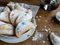 Cassatelle siciliane al forno, dolcetti dorati cosparsi di zucchero a velo e decorati con coriandoli colorati, pronti per essere gustati.