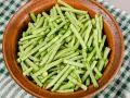 Fagiolini freschi, tagliati e pronti per essere cucinati in umido, in una ciotola di terracotta su una tovaglia a quadri verdi.