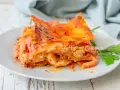 Una fetta di lasagna di mare napoletana, ricca e saporita, servita su un piatto bianco con un rametto di prezzemolo.
