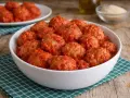 Un primo piatto invitante: polpette di pane al sugo, morbide e saporite, servite in una ciotola bianca su un tovagliolo a quadretti verdi.
