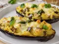 Melanzane a barchetta ripiene di un gustoso impasto e formaggio filante, guarnite con foglie di basilico fresco.