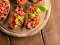Bruschette veloci per aperitivo: fette di pane tostato con pomodoro fresco a cubetti e basilico, pronte per essere gustate.
