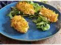 Tre croccanti polpette di patate impanate con fiocchi di mais, servite su un letto di insalata fresca su un piatto blu.