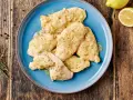 Delizioso petto di pollo in salsa cremosa, guarnito con erbe aromatiche e servito su un piatto blu. Accanto, limone e pepe nero.