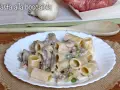 Piatto di pasta alla boscaiola con funghi, piselli e salsiccia, servita su un piatto bianco bordato.
