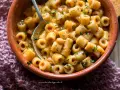 Un piatto invitante di pasta e fagioli estiva, condita con erbe fresche, servita in una ciotola di terracotta.