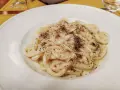 Pici cacio e pepe, un classico piatto romano, servito in un piatto bianco, con abbondante pepe nero macinato.