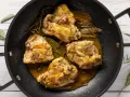Cosce di pollo in padella, dorate e succulente, con erbe aromatiche e un sughetto invitante.
