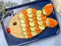 Un simpatico pesce finto ricetta, con corpo di purè, scaglie di cetriolo e carota, occhio d'oliva e bocca di peperone rosso.