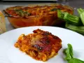 Una fetta di parmigiana di zucchine alla siciliana, dorata e succulenta, accanto a zucchine fresche e pane casereccio.