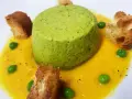 Sformato di piselli verde brillante su crema gialla, guarnito con piselli freschi e crostini dorati.