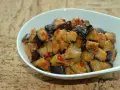 Melanzane al microonde, tagliate a cubetti e condite con pomodoro e spezie, servite in una ciotola bianca.