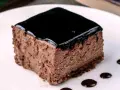 Un delizioso semifreddo al cioccolato, con una lucida glassa scura e gocce di salsa al cioccolato sul piatto bianco.