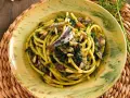 Un piatto di pasta con le sarde, condita con finocchietto selvatico, pinoli e uvetta, servita in un piatto decorato.