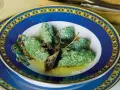 Strangolapreti alla trentina, verdi e saporiti, serviti in un piatto blu decorato con burro fuso e parmigiano.