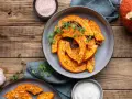 Fette di zucca in agrodolce in padella, condite con erbe aromatiche e servite su un piatto grigio, con contorno di aglio e sale rosa.