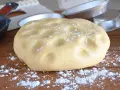 Impasto di pasta frolla con olio, pronto per essere lavorato. Si intravedono stampi per torte e utensili da cucina.