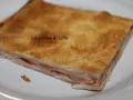 Una fetta di torta salata prosciutto e formaggio, con pasta sfoglia dorata e ripieno filante.
