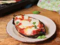 Melanzane alla pizzaiola appena sfornate, con mozzarella filante e basilico fresco su un piatto rustico.