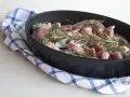 Pezzi di coniglio crudo in una teglia, pronti per essere cucinati al forno con rosmarino, salvia e aglio.