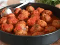 Un tegame pieno di polpette al sugo, pronte per essere gustate. Un cucchiaio d'argento è appoggiato sul bordo, invitando a servirle.