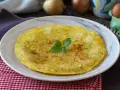 Una dorata frittata di cipolle, guarnita con basilico fresco, servita su un piatto bianco.