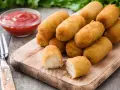 Crocchette di patate dorate e croccanti, servite su un tagliere di legno con ketchup e una forchetta.