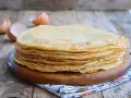Pila di crepes dorate, perfette per una crepes ricetta senza burro. Guscio d'uovo sullo sfondo.