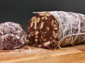 Salame al cioccolato vegano, un dolce goloso con biscotti e frutta secca, spolverato di zucchero a velo.