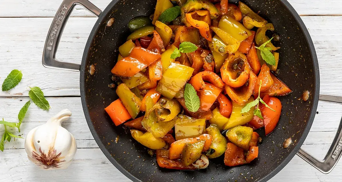 Peperoni in padella, colorati e succosi, con foglie di menta fresca e uno spicchio d'aglio.