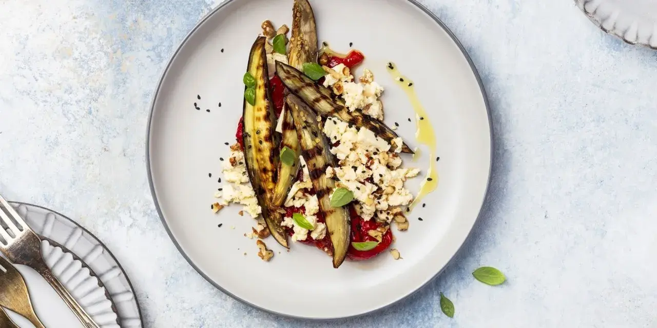 Deliziosa insalata di melanzane grigliate con feta sbriciolata, pomodoro, noci e semi di sesamo nero, condita con olio d'oliva.