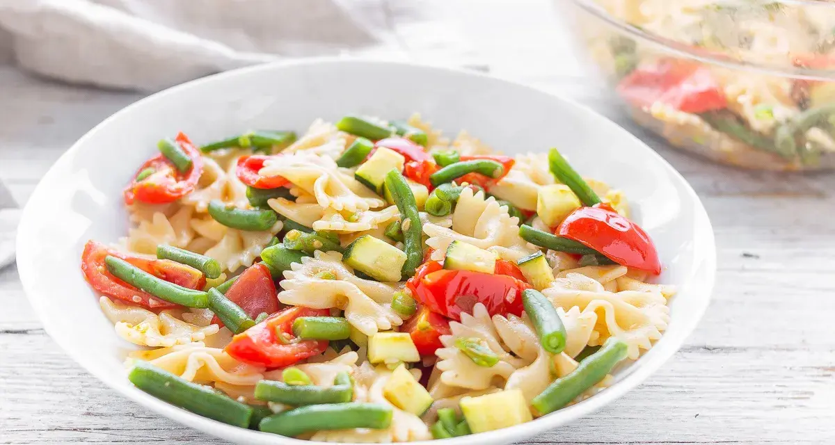 Un piatto invitante di pasta fredda vegana con farfalle, pomodorini, zucchine e fagiolini. Perfetta per un pasto leggero e gustoso.